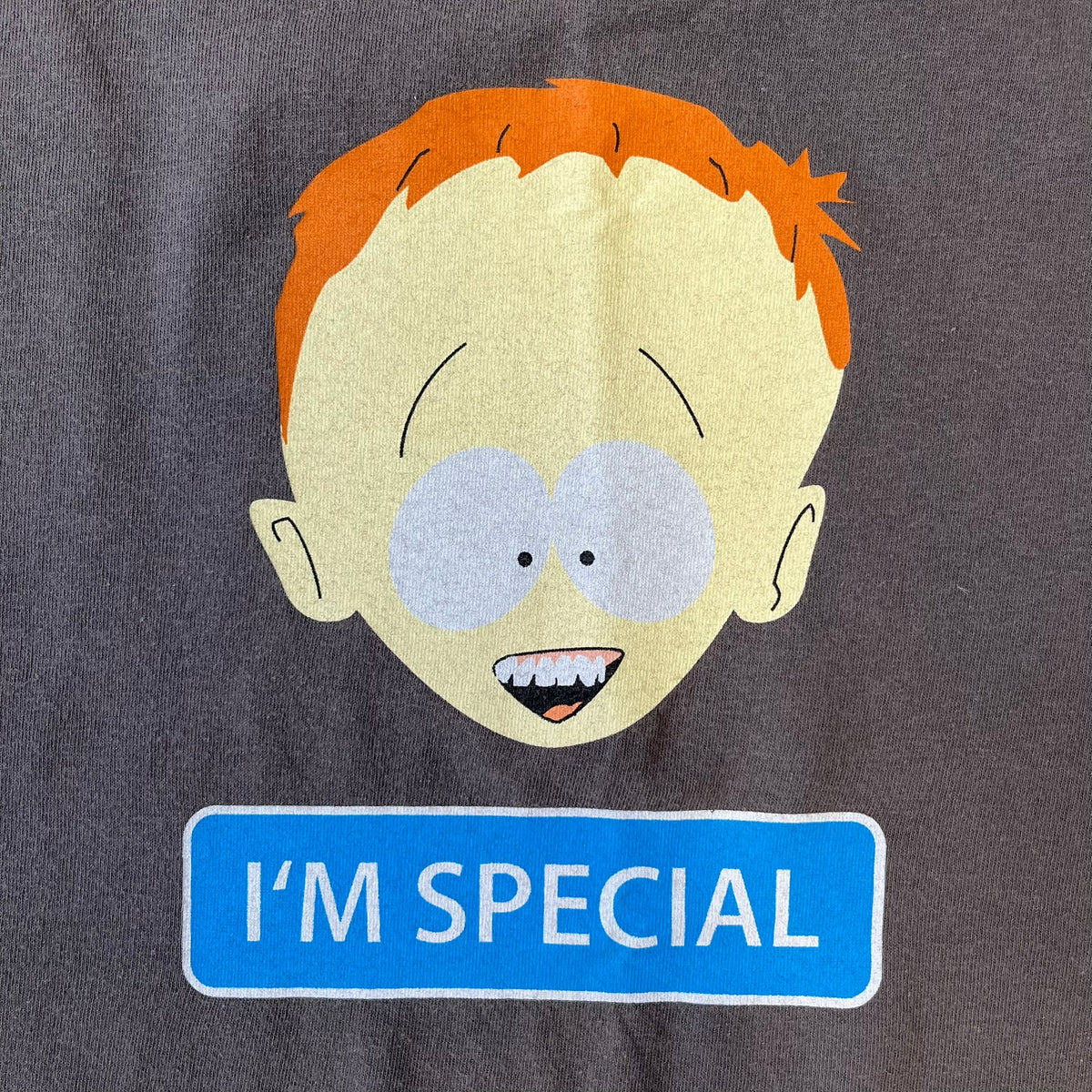 South Park 2008 Timmy “I’m Special” Tee features a grey T-shirt with a front graphic of Timmy’s face above a blue bar with white “I’m Special” text. The back features a blue and white wheelchair-accessibility sign graphic and 4 main characters white outlines with small 2008 licensing and Comedy Central details printed underneath.