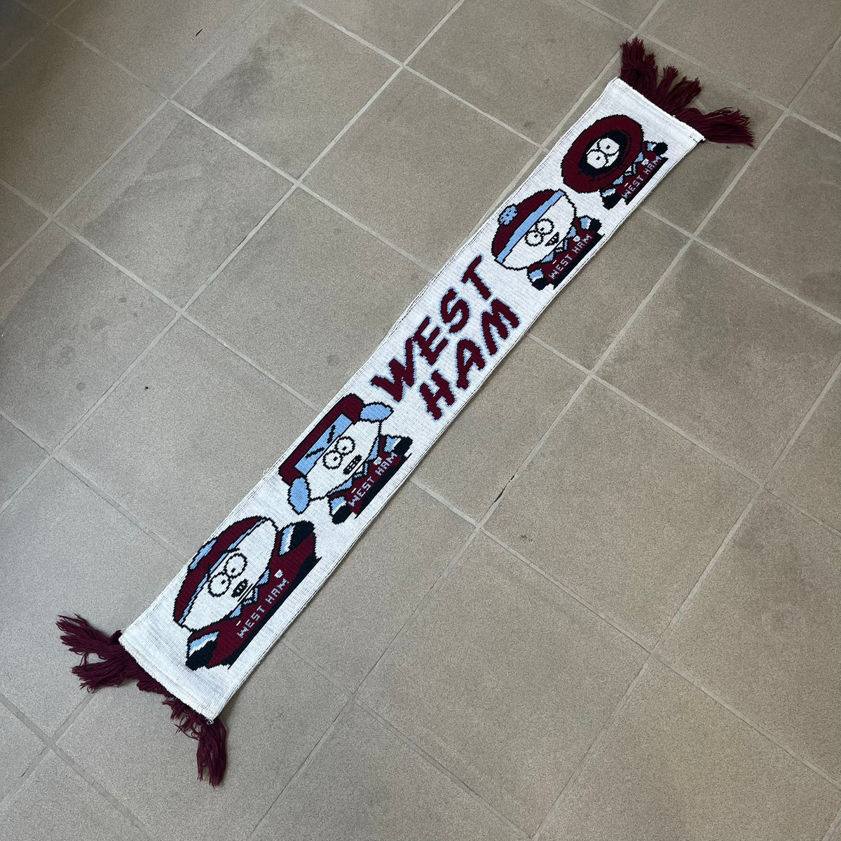 Vintage South Park West Ham 1990's Football Scarf in white and burgundy with fringe / tassels, featuring South Park characters including Kenny, Cartman, Kyle and Stan dressed in West Ham kits. The character graphics appear on both sides of the scarf, with consistent coloring in Burgundy and light blue.
