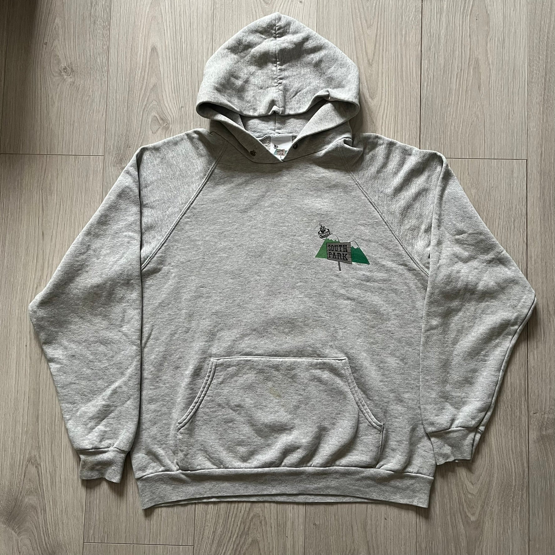 South Park “Stitched Up Kenny” Hoodie from 1998 in Gray, made on a Screen Stars blank. Features a small South Park logo on the chest and a large stitched-up Kenny graphic on the back. Vintage licensed piece from the show’s early era.