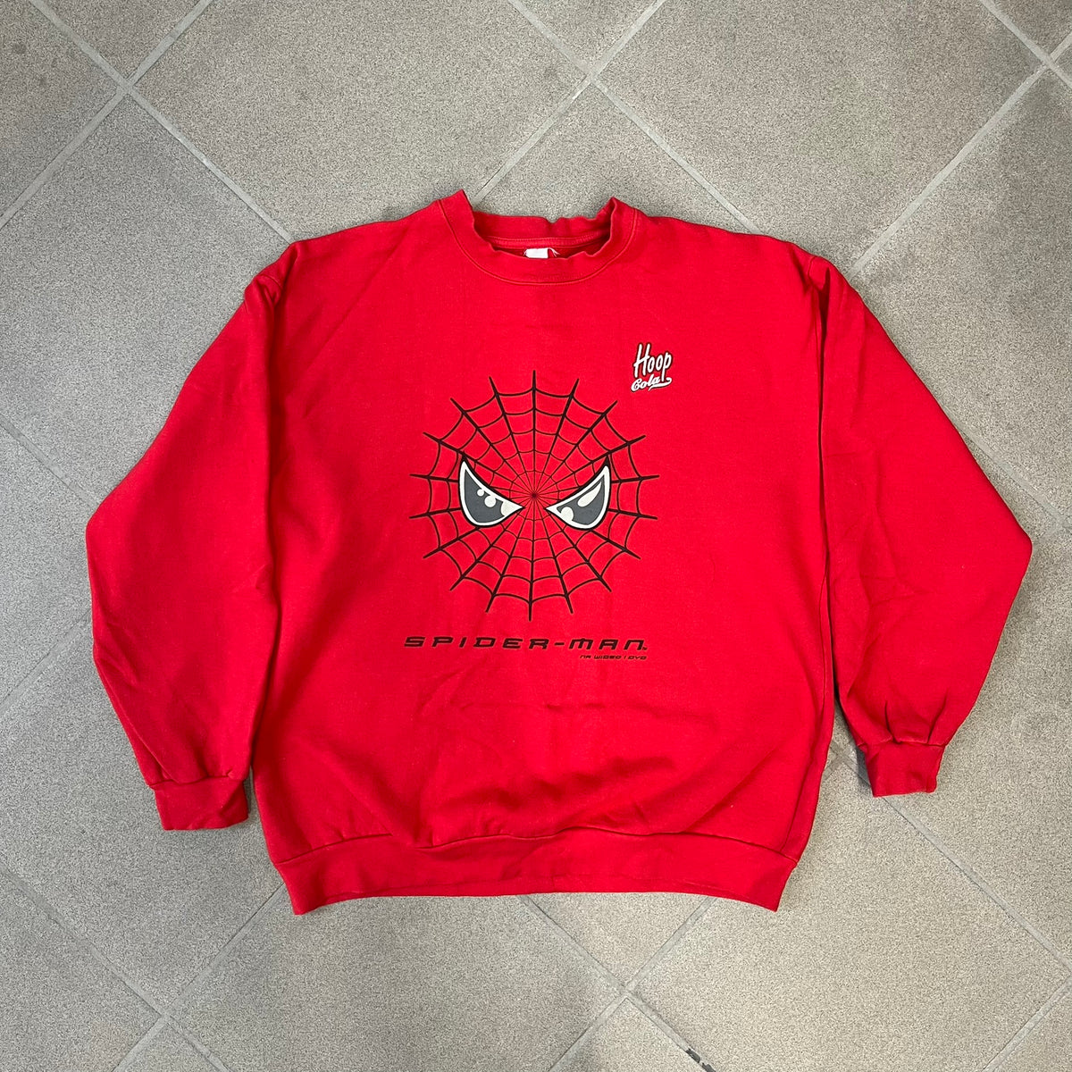Spider-Man 2002 Hoop Cola Promo Red Crewneck is a rare Poland-exclusive crewneck made for the cross-promotional campaign between Hoop Cola and Warner Bros for the Spider-Man (2002) film. It was never sold in stores and was given out only as a prize in the SMS code contest. The cotton crewneck features web with eyes graphic in the middle, Spider-Man logo under and a Hoop Cola logo above.