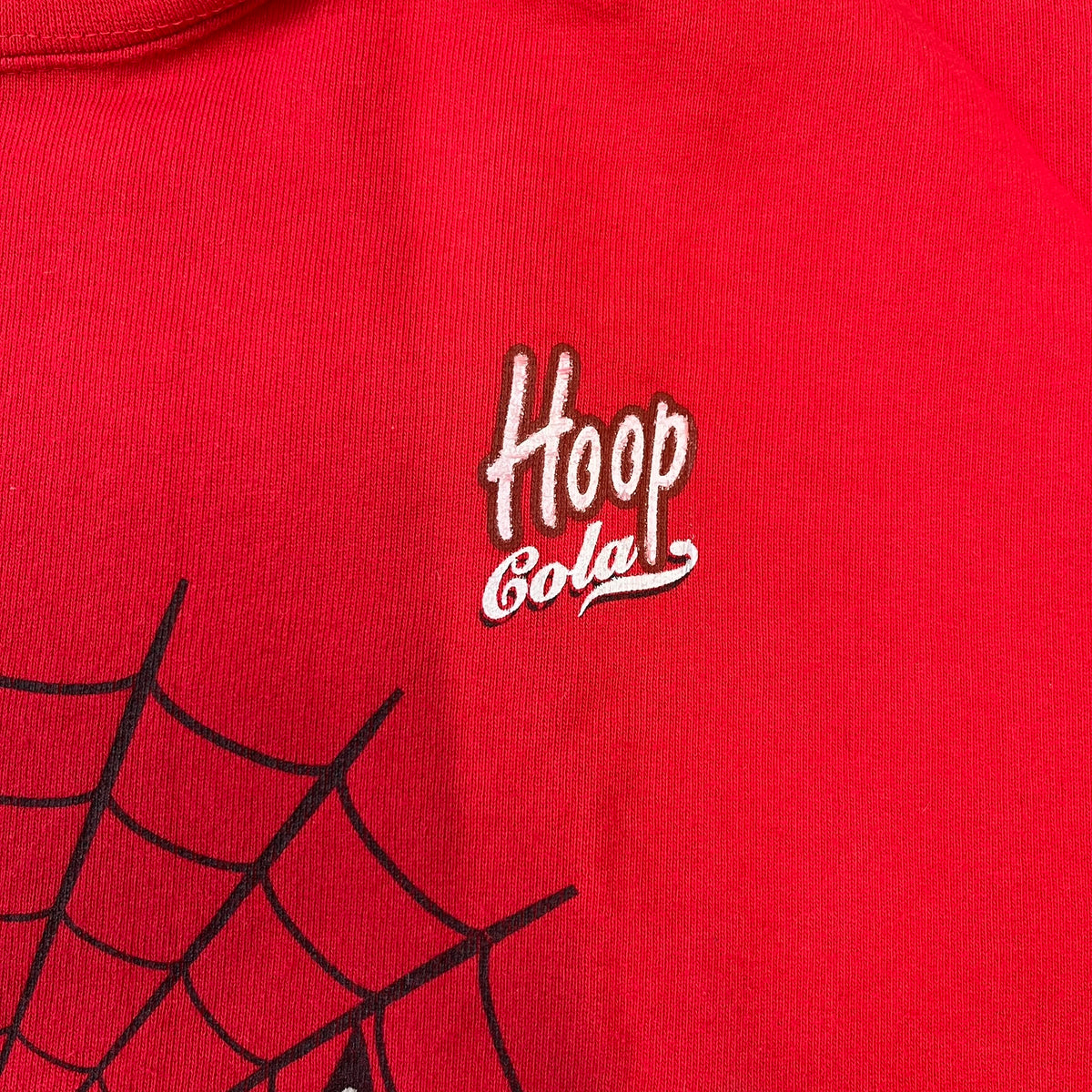 Spider-Man 2002 Hoop Cola Promo Red Crewneck is a rare Poland-exclusive crewneck made for the cross-promotional campaign between Hoop Cola and Warner Bros for the Spider-Man (2002) film. It was never sold in stores and was given out only as a prize in the SMS code contest. The cotton crewneck features web with eyes graphic in the middle, Spider-Man logo under and a Hoop Cola logo above.