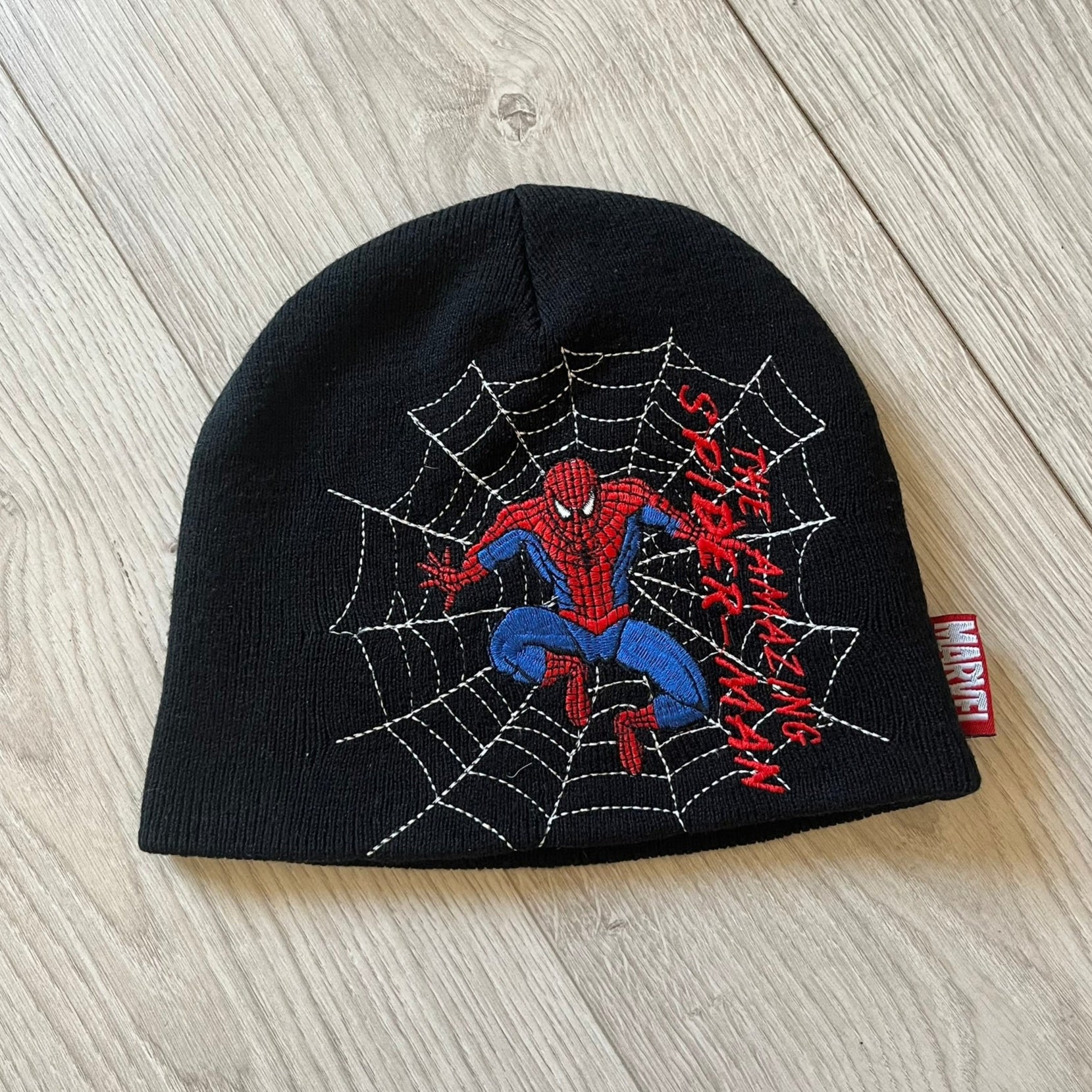 Black beanie with Spider-Man design on a wooden surface