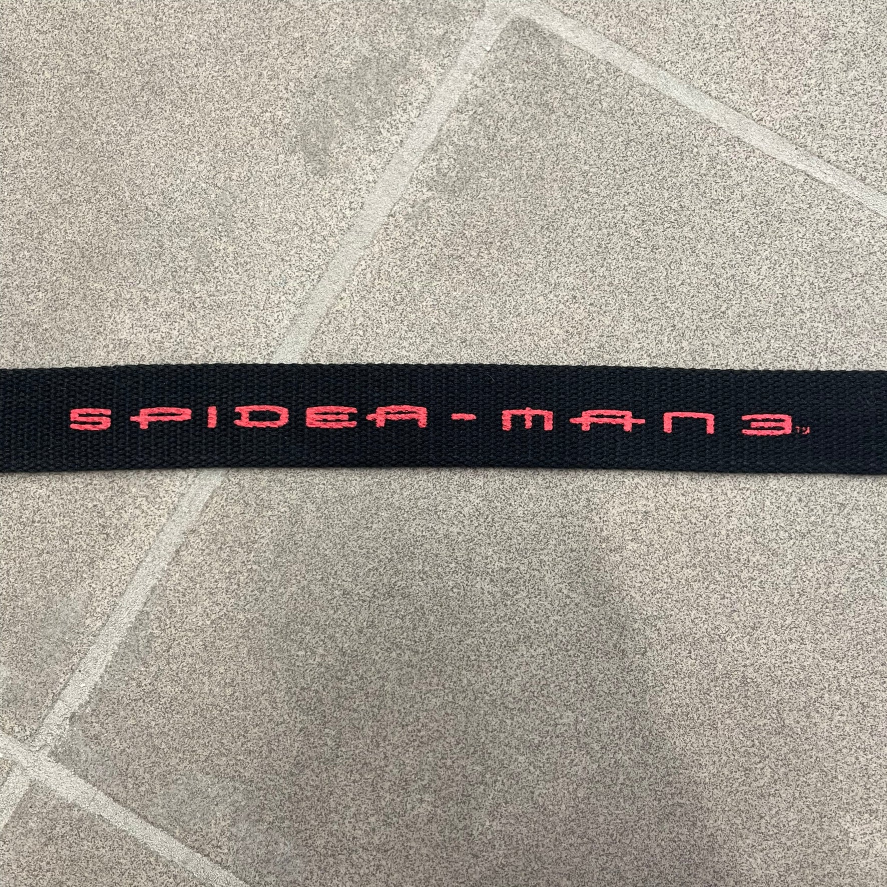 Spider-Man 3 2007 Black Belt is a black adjustable belt featuring repeated horizontal red Spider-Man 3 logo graphics across the strap. The belt has a red metal buckle with a Spider-Man graphic on the front showing him swinging. It includes a metal belt tip finish and a regulated sizing system for adjustment.
