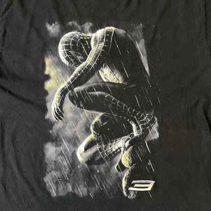 Spider-Man 3 Blacksuit 2007 Poster Tee features a black 100% cotton T-shirt with a large front graphic of Spider-Man crouching in the black suit in the rain. A “3” is printed in the bottom-right corner of the graphic. The shirt has a 2007 licensed black neck tag.

