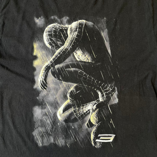 Spider-Man 3 Blacksuit 2007 Poster Tee features a black 100% cotton T-shirt with a large front graphic of Spider-Man crouching in the black suit in the rain. A “3” is printed in the bottom-right corner of the graphic. The shirt has a 2007 licensed black neck tag.
