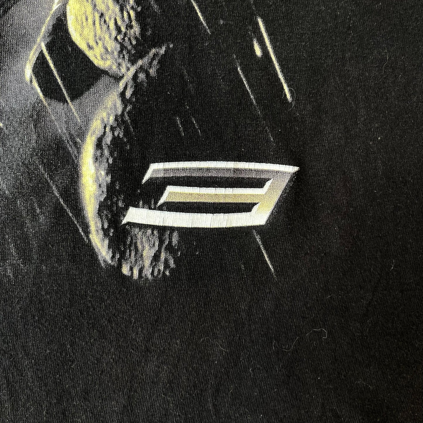 Spider-Man 3 Blacksuit 2007 Poster Tee features a black 100% cotton T-shirt with a large front graphic of Spider-Man crouching in the black suit in the rain. A “3” is printed in the bottom-right corner of the graphic. The shirt has a 2007 licensed black neck tag.
