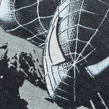 Spider-Man 3 Promo 2007 Black Tee is a black short-sleeve T-shirt with an original Spider-Man 3 neck tag. The front features a crawling black-suit Spider-Man graphic with a painted-style “3” beneath, set against a city background in white, grey, and black tones. The number “3” and the character’s eyes include a subtle glitter finish.
