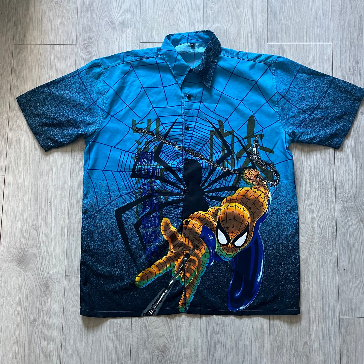 Blue Spider-Man button-up shirt featuring an all-over web print and mirrored graphics of Spider-Man shooting webs on both sides. Centered Spider-Man logo completes the great design. A striking, comic-inspired piece perfect for fans and collectors.