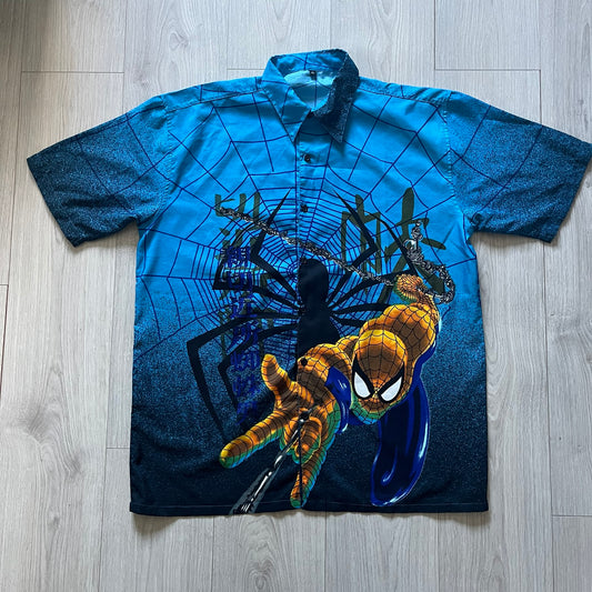 Blue Spider-Man button-up shirt featuring an all-over web print and mirrored graphics of Spider-Man shooting webs on both sides. Centered Spider-Man logo completes the great design. A striking, comic-inspired piece perfect for fans and collectors.