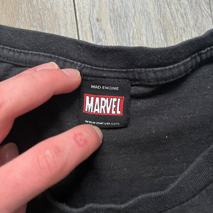 Spider-Man Marvel Timestorm 2009–2099 Tee is a black T-shirt featuring the Timestorm 2009–2099 cover graphic. The print shows Spider-Man half in his classic design and half in the 2099 version, sitting with a blurred green city background. Made by Marvel Mad Engine, the shirt highlights the multiversal crossover design.