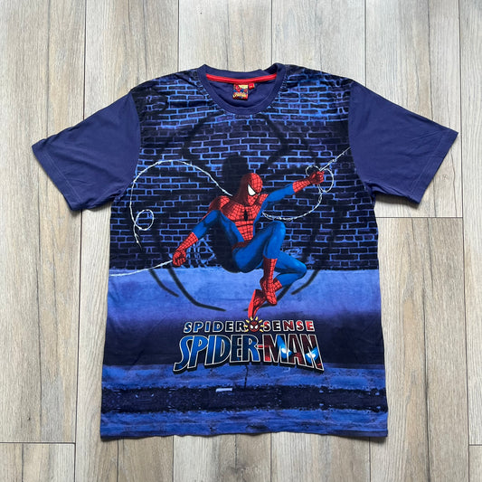 Spider-Man “Spider Sense” 2010 AOP Tee is a navy all-over print style T-shirt featuring a large front graphic of cartoon Spider-Man swinging in front of a brick wall with a black Spider-Man logo mural. Below the artwork is detailed “Spider Sense Spider-Man” text. The back features a simple outlined white Spider-Man logo near the upper back. Produced under license by Contrast with 2010 Marvel licensing and a detailed branded neck tag.
