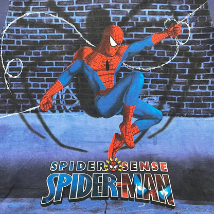 Spider-Man “Spider Sense” 2010 AOP Tee is a navy all-over print style T-shirt featuring a large front graphic of cartoon Spider-Man swinging in front of a brick wall with a black Spider-Man logo mural. Below the artwork is detailed “Spider Sense Spider-Man” text. The back features a simple outlined white Spider-Man logo near the upper back. Produced under license by Contrast with 2010 Marvel licensing and a detailed branded neck tag.
