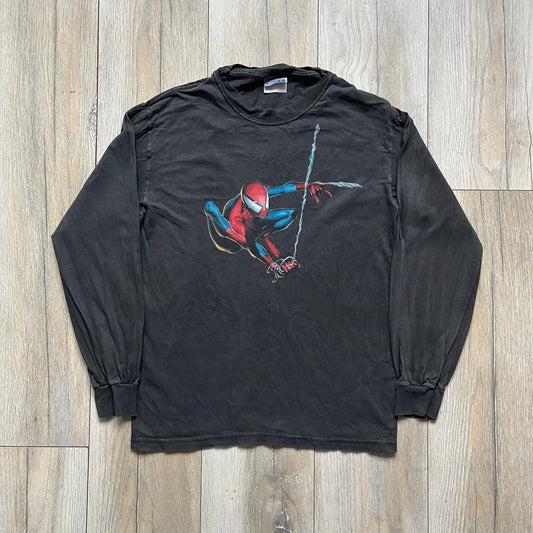 Spider-Man Swinging 2003 Washed Longsleeve is a washed black and dark gray cotton long-sleeve shirt made on a Hanes Beefy-T blank. The front features a large detailed comic-style Spider-Man graphic in red and blue, showing the character swinging in motion. Made from 100% cotton with a faded vintage finish.
