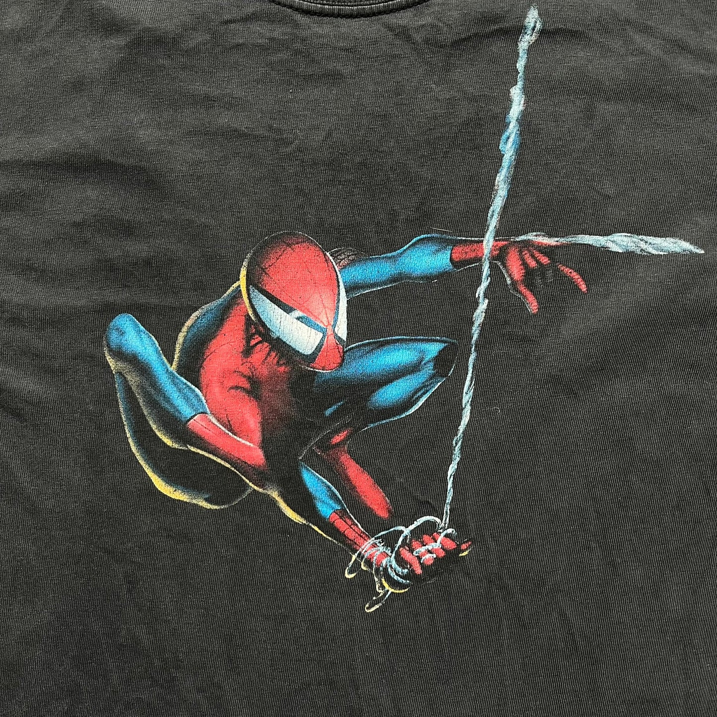 Spider-Man Swinging 2003 Washed Longsleeve is a washed black and dark gray cotton long-sleeve shirt made on a Hanes Beefy-T blank. The front features a large detailed comic-style Spider-Man graphic in red and blue, showing the character swinging in motion. Made from 100% cotton with a faded vintage finish.
