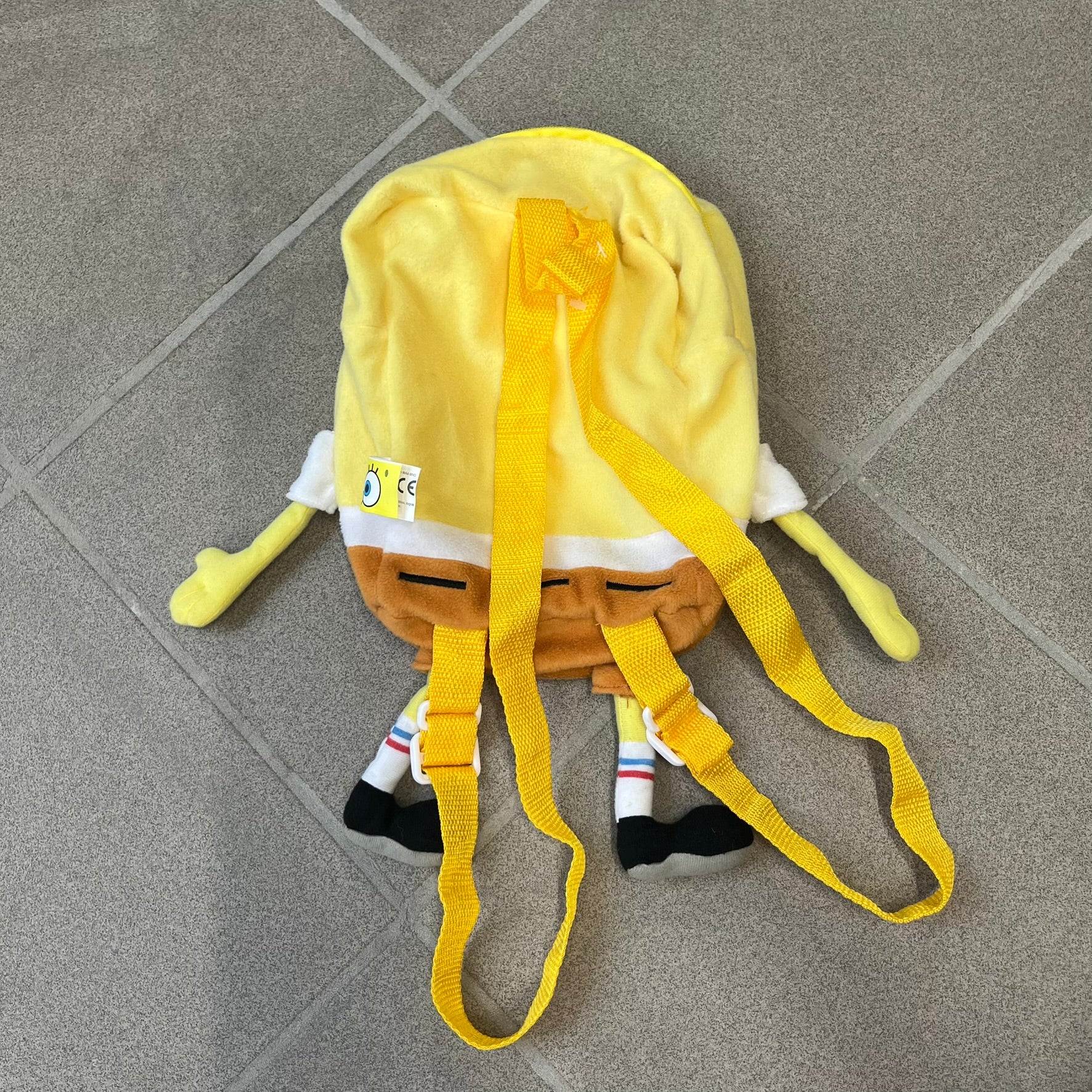 SpongeBob SquarePants 2010 Backpack is designed in the shape of SpongeBob’s body with embroidered facial details, a 3D nose, and loose hanging arms and legs. It features one main compartment and a yellow 2010 licensed tag on the side.
