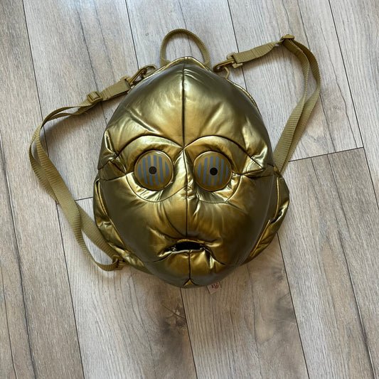 Star Wars 1990s C-3PO Head Backpack is a novelty backpack shaped like the head of C-3PO. It features a metallic gold finish with detailed sculpted paneling and plastic lens-style eyes for a robotic look. The bag includes a 1990s Star Wars red licensed tag and a single main compartment.