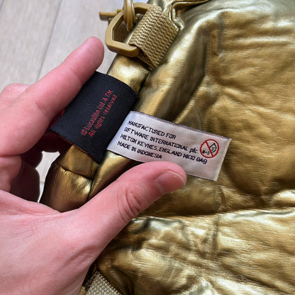 Star Wars 1990s C-3PO Head Backpack is a novelty backpack shaped like the head of C-3PO. It features a metallic gold finish with detailed sculpted paneling and plastic lens-style eyes for a robotic look. The bag includes a 1990s Star Wars red licensed tag and a single main compartment.
