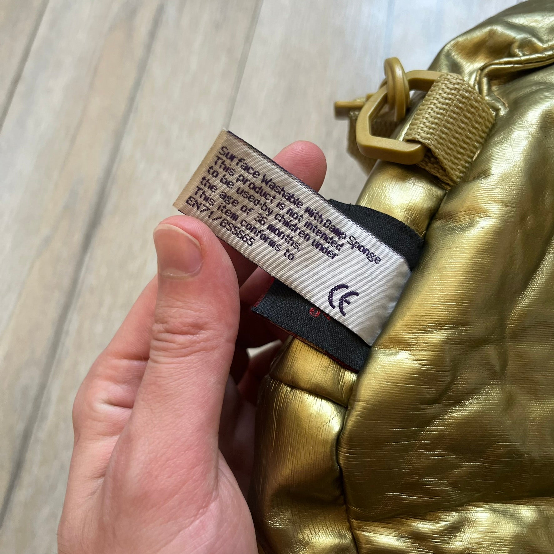 Star Wars 1990s C-3PO Head Backpack is a novelty backpack shaped like the head of C-3PO. It features a metallic gold finish with detailed sculpted paneling and plastic lens-style eyes for a robotic look. The bag includes a 1990s Star Wars red licensed tag and a single main compartment.