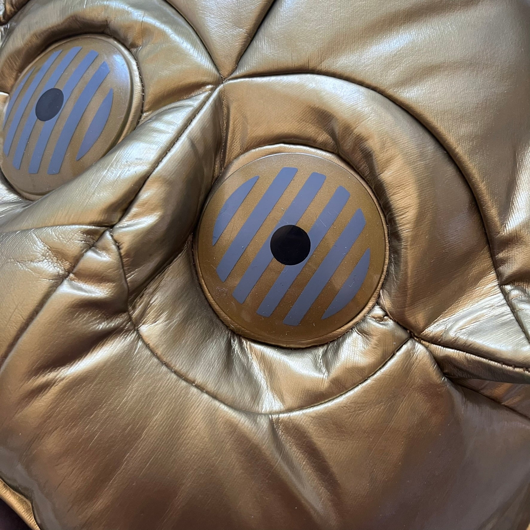 Star Wars 1990s C-3PO Head Backpack is a novelty backpack shaped like the head of C-3PO. It features a metallic gold finish with detailed sculpted paneling and plastic lens-style eyes for a robotic look. The bag includes a 1990s Star Wars red licensed tag and a single main compartment.