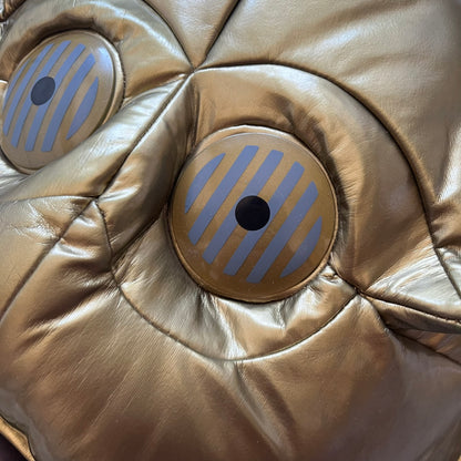 Star Wars 1990s C-3PO Head Backpack is a novelty backpack shaped like the head of C-3PO. It features a metallic gold finish with detailed sculpted paneling and plastic lens-style eyes for a robotic look. The bag includes a 1990s Star Wars red licensed tag and a single main compartment.