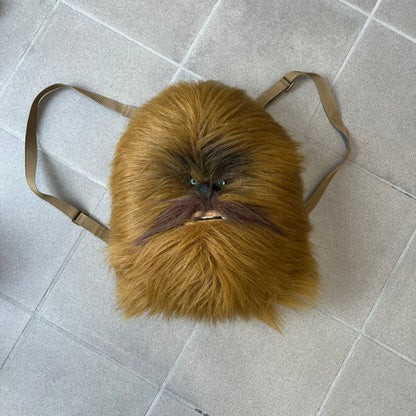 Star Wars 1990s Chewbacca Head Backpack is a novelty bag designed in the shape of Chewbacca’s head. The exterior features a furry construction with plastic eyes and a leather-like nose and mouth. It includes an adjustable shoulder straps, a single main compartment and a red Star Wars licensed tag.