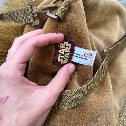 Star Wars 1990s Chewbacca Head Backpack is a novelty bag designed in the shape of Chewbacca’s head. The exterior features a furry construction with plastic eyes and a leather-like nose and mouth. It includes an adjustable shoulder straps, a single main compartment and a red Star Wars licensed tag.