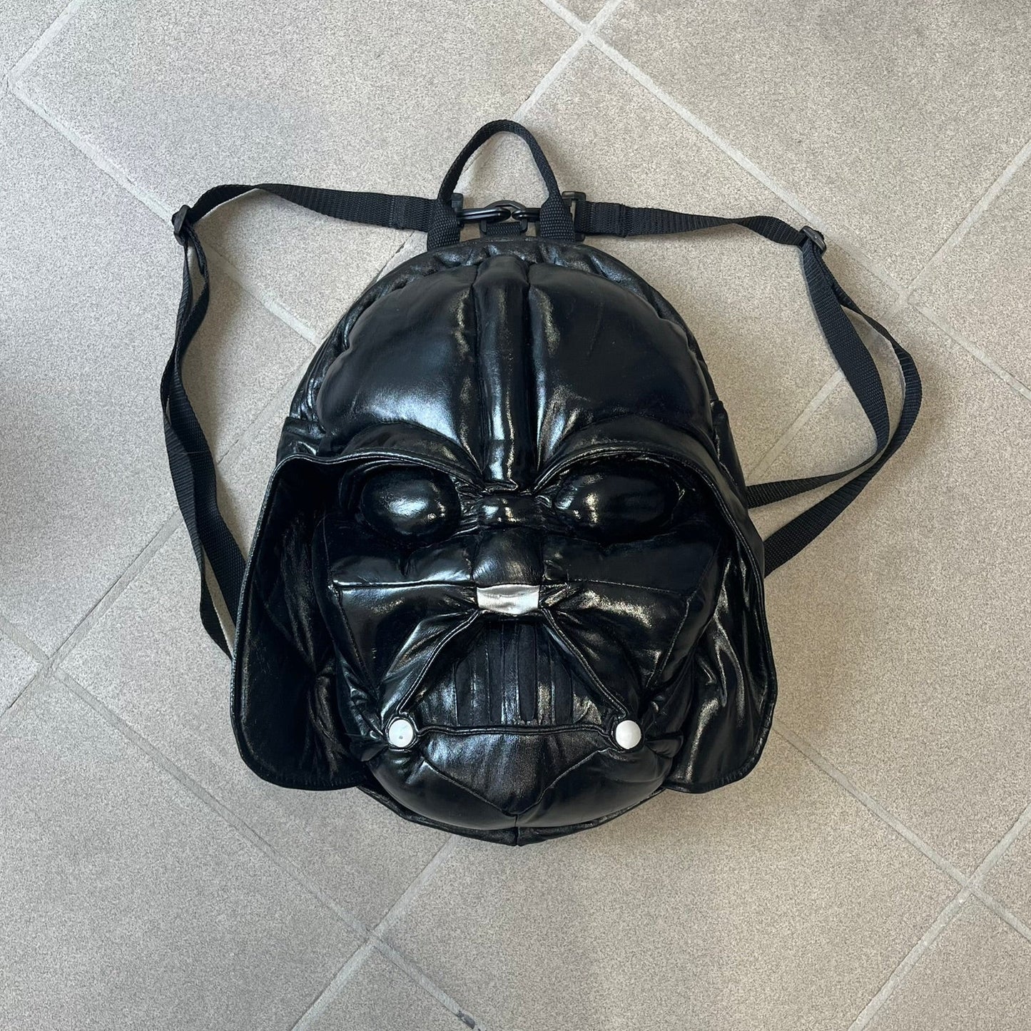 Star Wars 1990s Darth Vader Head Backpack is a vintage backpack shaped like Darth Vader’s helmet. It is finished in shiny black with molded plastic details recreating the character’s mask and helmet. The bag has one main compartment and includes a red Star Wars licensed tag from the 1990s.