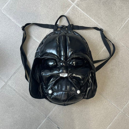 Star Wars 1990s Darth Vader Head Backpack is a vintage backpack shaped like Darth Vader’s helmet. It is finished in shiny black with molded plastic details recreating the character’s mask and helmet. The bag has one main compartment and includes a red Star Wars licensed tag from the 1990s.