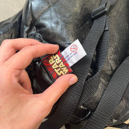 Star Wars 1990s Darth Vader Head Backpack is a vintage backpack shaped like Darth Vader’s helmet. It is finished in shiny black with molded plastic details recreating the character’s mask and helmet. The bag has one main compartment and includes a red Star Wars licensed tag from the 1990s.