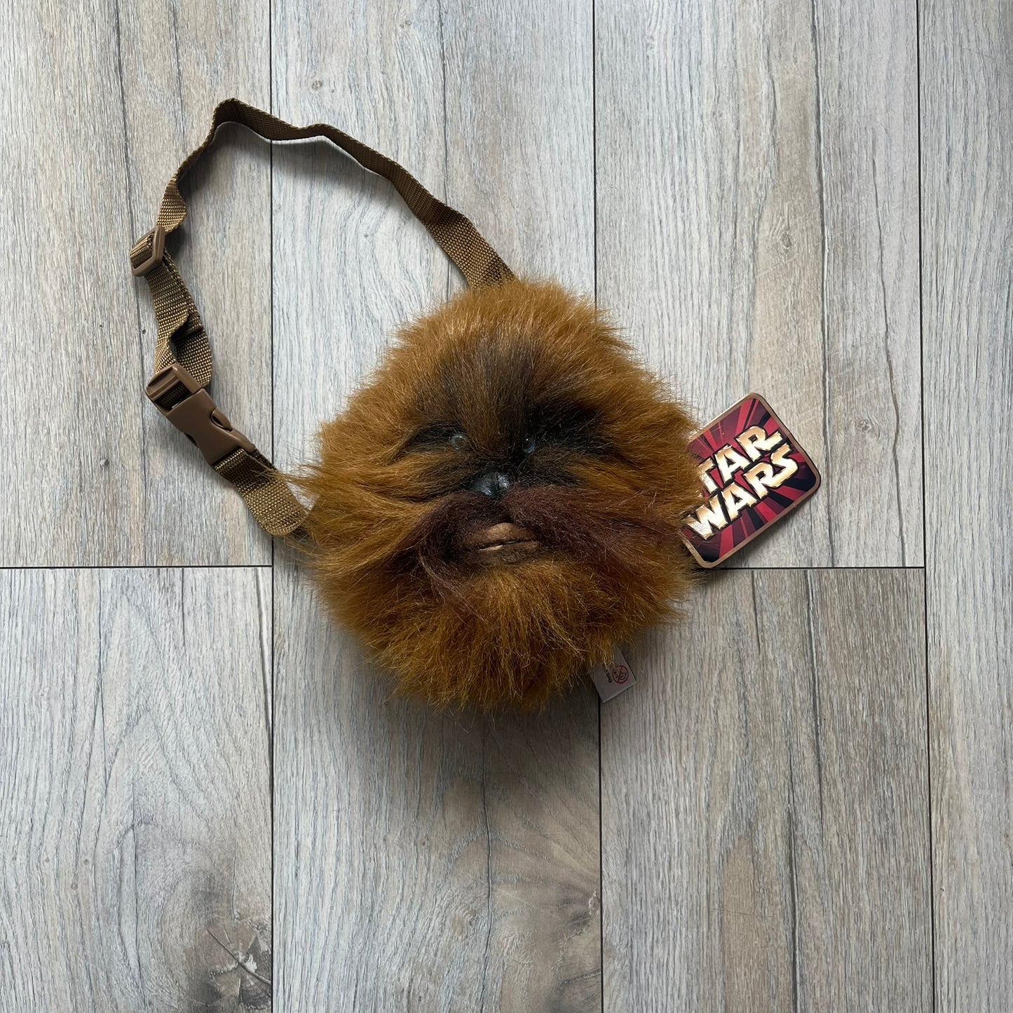 Star Wars 1990s Chewbacca Head Shoulder Bag is a novelty shoulder bag designed in the shape of Chewbacca’s head. The exterior features a furry construction with plastic eyes and a leather-like nose and mouth. It includes an adjustable shoulder strap, a single main compartment, a red Star Wars licensed tag, and the original paper tag.