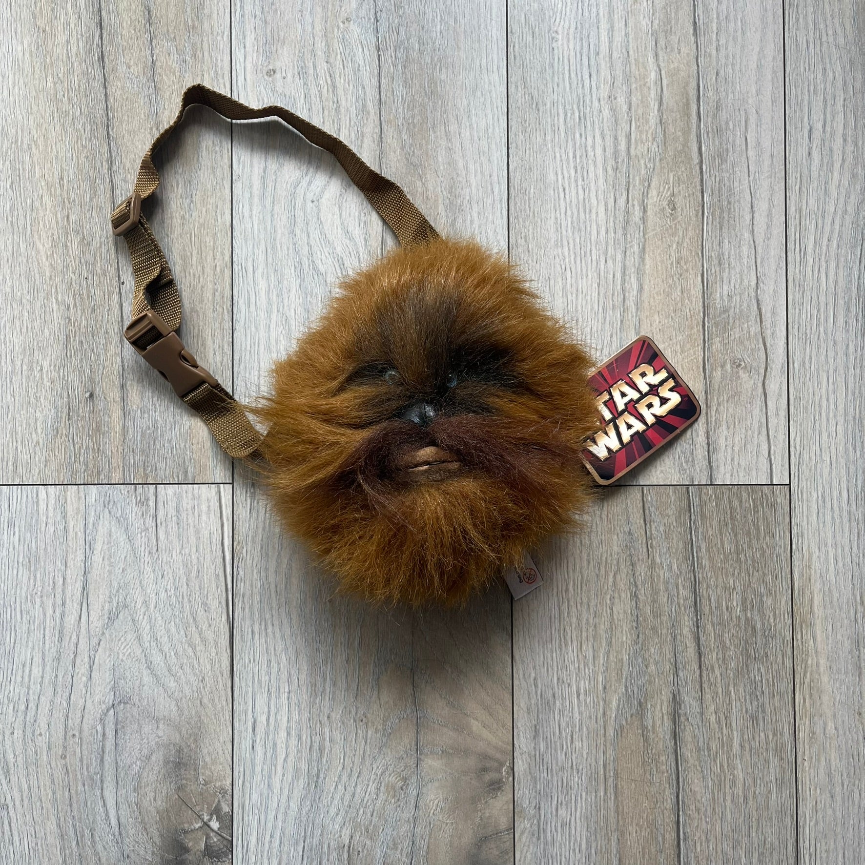 Star Wars 1990s Chewbacca Head Shoulder Bag is a novelty shoulder bag designed in the shape of Chewbacca’s head. The exterior features a furry construction with plastic eyes and a leather-like nose and mouth. It includes an adjustable shoulder strap, a single main compartment, a red Star Wars licensed tag, and the original paper tag.