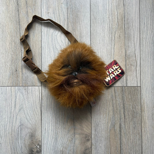 Star Wars 1990s Chewbacca Head Shoulder Bag is a novelty shoulder bag designed in the shape of Chewbacca’s head. The exterior features a furry construction with plastic eyes and a leather-like nose and mouth. It includes an adjustable shoulder strap, a single main compartment, a red Star Wars licensed tag, and the original paper tag.