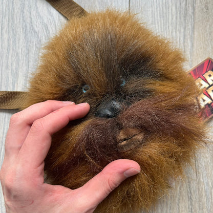 Star Wars 1990s Chewbacca Head Shoulder Bag is a novelty shoulder bag designed in the shape of Chewbacca’s head. The exterior features a furry construction with plastic eyes and a leather-like nose and mouth. It includes an adjustable shoulder strap, a single main compartment, a red Star Wars licensed tag, and the original paper tag.