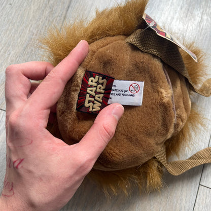Star Wars 1990s Chewbacca Head Shoulder Bag is a novelty shoulder bag designed in the shape of Chewbacca’s head. The exterior features a furry construction with plastic eyes and a leather-like nose and mouth. It includes an adjustable shoulder strap, a single main compartment, a red Star Wars licensed tag, and the original paper tag.