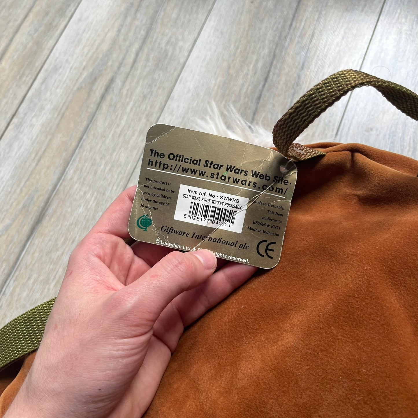 Star Wars 1990s Ewok Wicket Head Backpack is a plush backpack designed in the shape of the Ewok character Wicket W. Warrick. The bag features a brown Ewok face with a white beard and a brown hood, along with green camo-style shoulder straps. It includes a 1990s Star Wars neck tag and original paper tag.