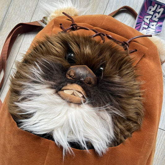 Star Wars 1990s Ewok Wicket Head Backpack is a plush backpack designed in the shape of the Ewok character Wicket W. Warrick. The bag features a brown Ewok face with a white beard and a brown hood, along with green camo-style shoulder straps. It includes a 1990s Star Wars neck tag and original paper tag.