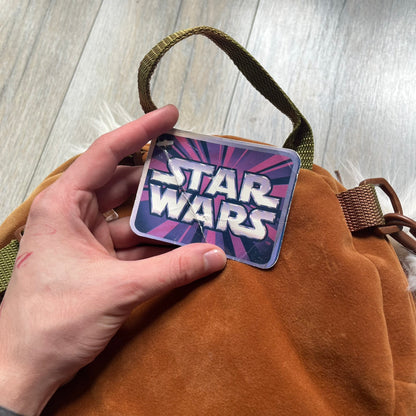 Star Wars 1990s Ewok Wicket Head Backpack is a plush backpack designed in the shape of the Ewok character Wicket W. Warrick. The bag features a brown Ewok face with a white beard and a brown hood, along with green camo-style shoulder straps. It includes a 1990s Star Wars neck tag and original paper tag.