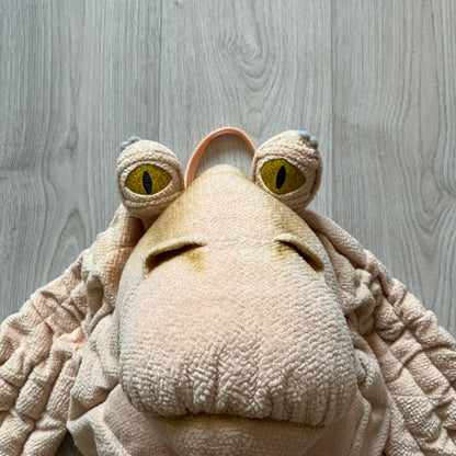 Vintage 1990s Star Wars backpack shaped like Jar Jar Binks’ head, complete with oversized ears for a playful, collectible design. This nostalgic piece captures the quirky charm of the character while offering functional storage. A rare, fun accessory for fans of classic Star Wars memorabilia.