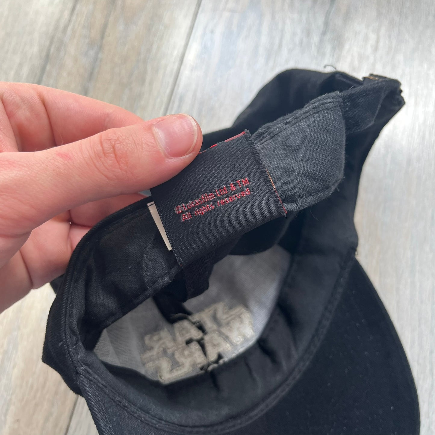 Star Wars Episode I 1990s Black Baseball Cap is a black cotton cap featuring embroidered Star Wars branding on the front in white and gray tones. Beneath it, a smaller “Episode I” embroidery is included for additional detailing. The interior includes a red Star Wars licensed tag, completing the official branded construction.