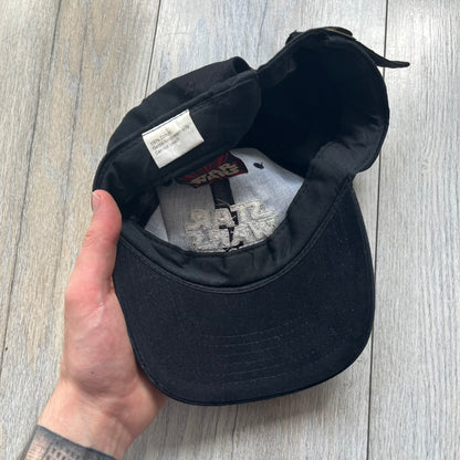 Star Wars Episode I 1990s Black Baseball Cap is a black cotton cap featuring embroidered Star Wars branding on the front in white and gray tones. Beneath it, a smaller “Episode I” embroidery is included for additional detailing. The interior includes a red Star Wars licensed tag, completing the official branded construction.