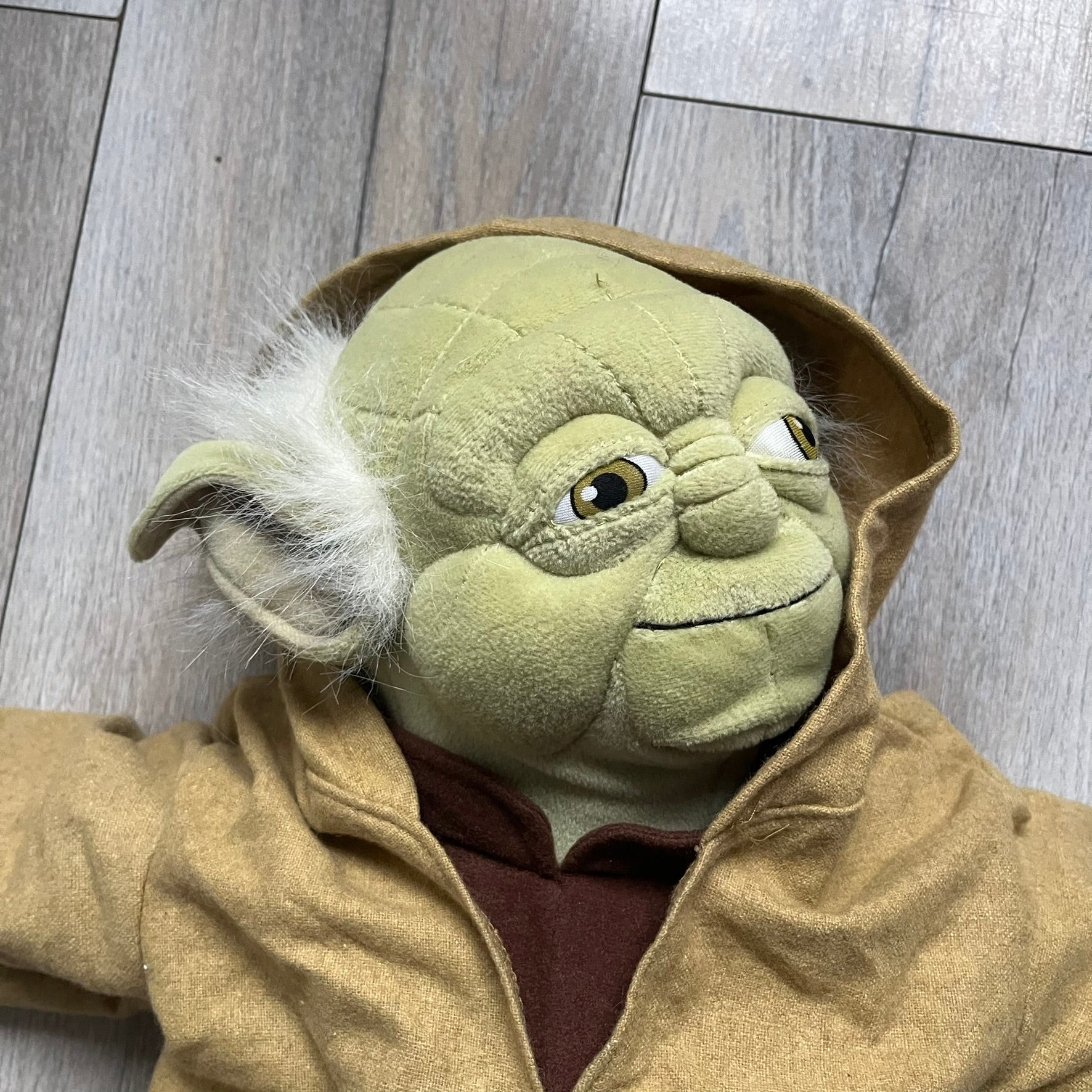 Star Wars Episode III Yoda 2006 Backpack is a character-shaped backpack featuring Yoda dressed in brown pants and a beige-yellow jacket with an attached hood. It includes two standard shoulder straps running from the hands to the feet, plus an additional stabilizing strap attached near the legs. The interior tag shows Star Wars Episode III: Revenge of the Sith branding with 2006 Lucasfilm licensing.