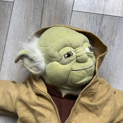 Star Wars Episode III Yoda 2006 Backpack is a character-shaped backpack featuring Yoda dressed in brown pants and a beige-yellow jacket with an attached hood. It includes two standard shoulder straps running from the hands to the feet, plus an additional stabilizing strap attached near the legs. The interior tag shows Star Wars Episode III: Revenge of the Sith branding with 2006 Lucasfilm licensing.