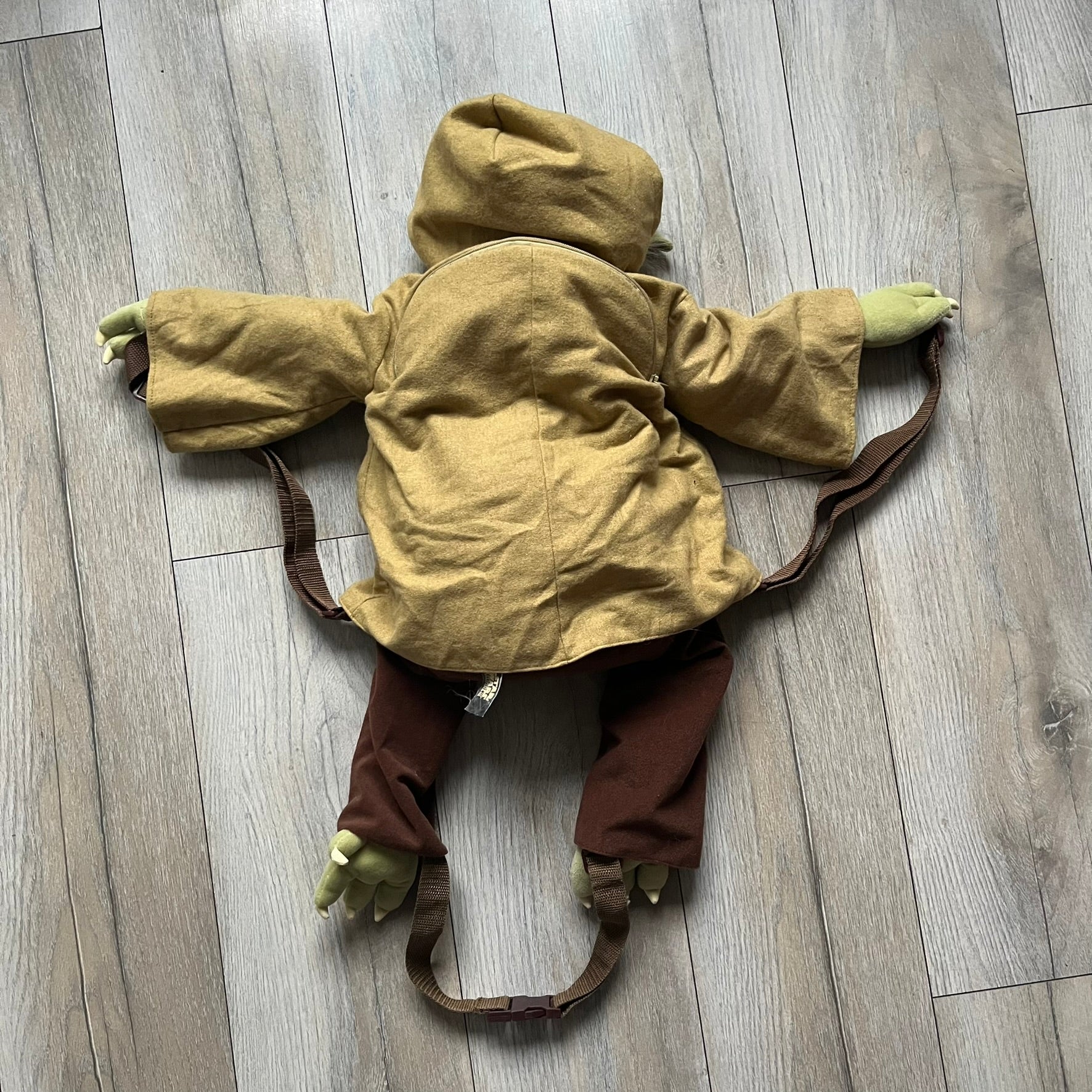 Star Wars Episode III Yoda 2006 Backpack is a character-shaped backpack featuring Yoda dressed in brown pants and a beige-yellow jacket with an attached hood. It includes two standard shoulder straps running from the hands to the feet, plus an additional stabilizing strap attached near the legs. The interior tag shows Star Wars Episode III: Revenge of the Sith branding with 2006 Lucasfilm licensing.