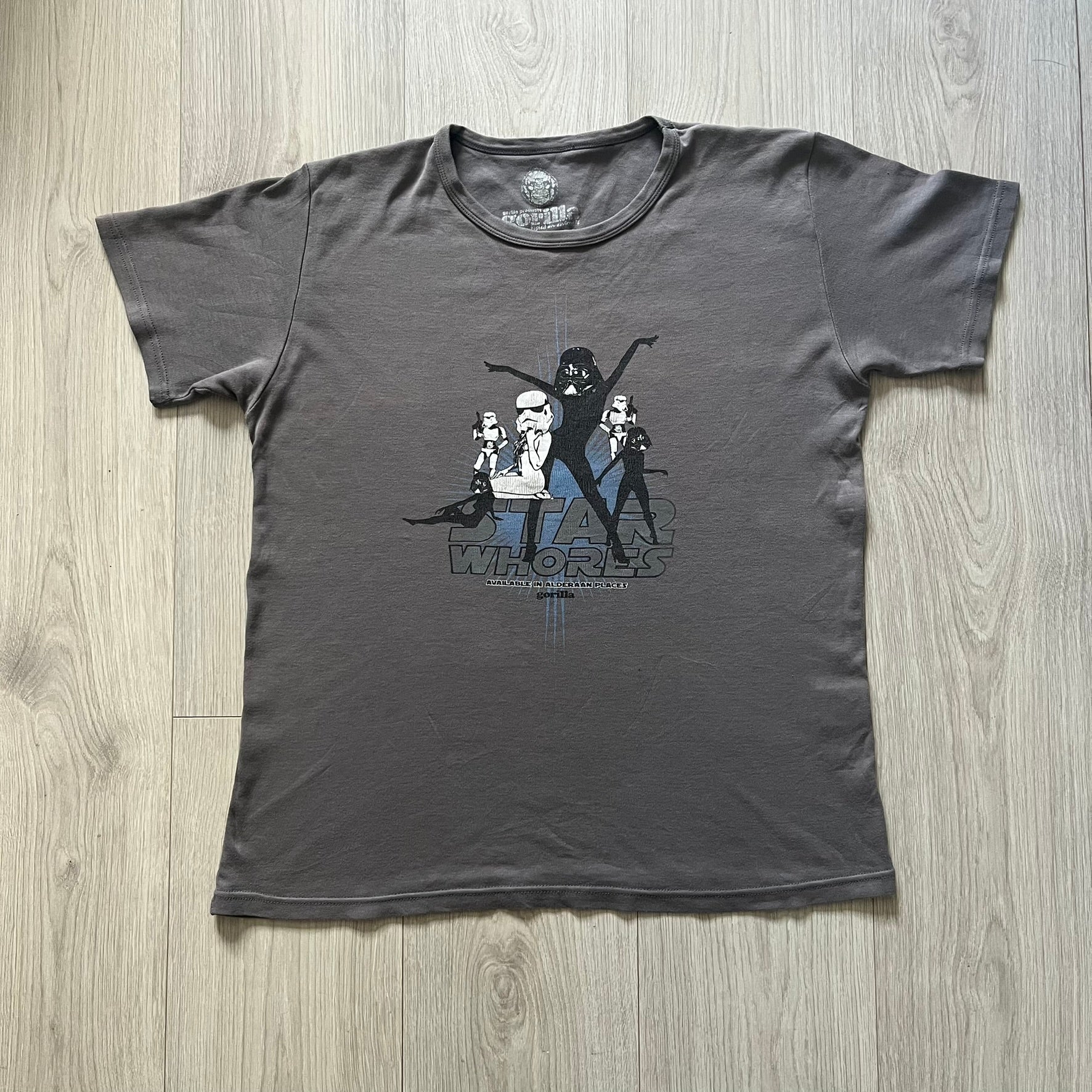 Gray Star Wh*res tee showcasing female figures in Stormtrooper and Vader masks. Logo sits prominently on the chest with witty “Available in Alderaan Places” tagline beneath. A perfect sci-fi parody tee.