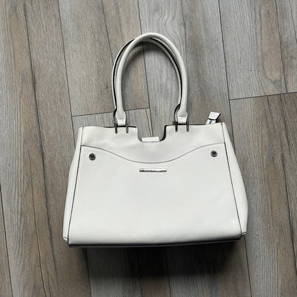 Steve Madden Removable Clutch White Handbag is a white leather tote featuring silver-tone hardware, including a front plaque and decorative buttons. The bag has two top handles and includes a removable inner clutch with silver Steve Madden branding. Designed for versatility, the clutch can be used separately or inside the main handbag.