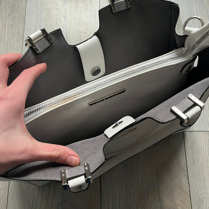 Steve Madden Removable Clutch White Handbag is a white leather tote featuring silver-tone hardware, including a front plaque and decorative buttons. The bag has two top handles and includes a removable inner clutch with silver Steve Madden branding. Designed for versatility, the clutch can be used separately or inside the main handbag.