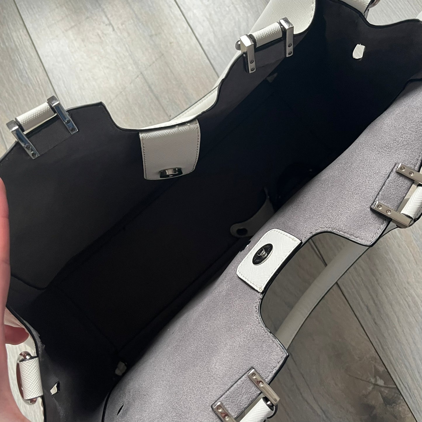 Steve Madden Removable Clutch White Handbag is a white leather tote featuring silver-tone hardware, including a front plaque and decorative buttons. The bag has two top handles and includes a removable inner clutch with silver Steve Madden branding. Designed for versatility, the clutch can be used separately or inside the main handbag.