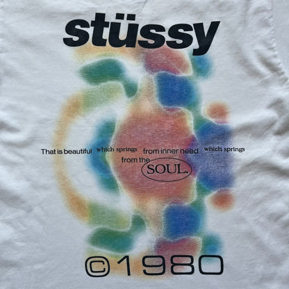 Stussy Soul 1980 White Tee is a white short-sleeve T-shirt released as part of a spring drop, made from soft cotton with a relaxed fit and ribbed collar. The front features a small Stussy logo print on the chest, while the back includes black Stussy text, a large multicolor central graphic, and “Copyright 1980” text at the bottom.