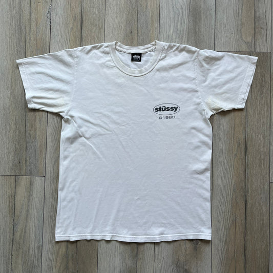 Stussy Soul 1980 White Tee is a white short-sleeve T-shirt released as part of a spring drop, made from soft cotton with a relaxed fit and ribbed collar. The front features a small Stussy logo print on the chest, while the back includes black Stussy text, a large multicolor central graphic, and “Copyright 1980” text at the bottom.