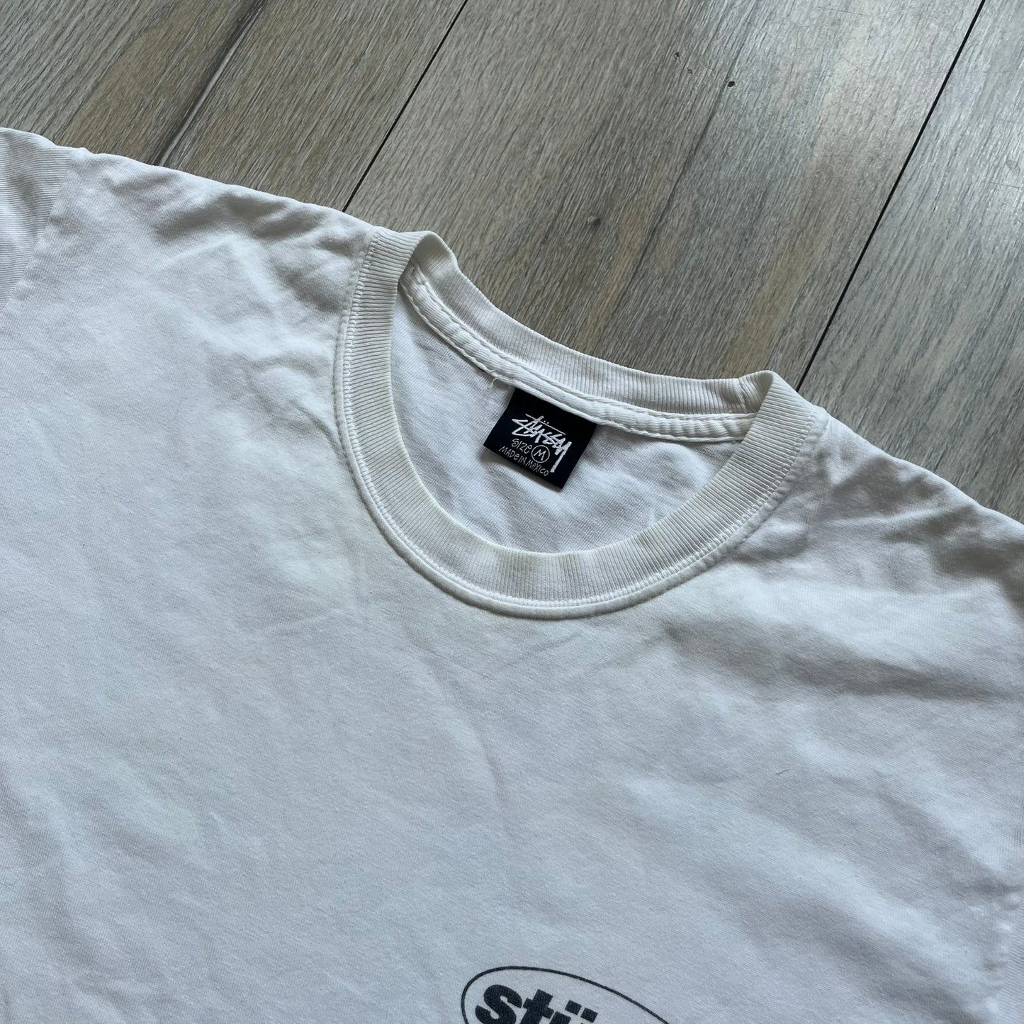 Stussy Soul 1980 White Tee is a white short-sleeve T-shirt released as part of a spring drop, made from soft cotton with a relaxed fit and ribbed collar. The front features a small Stussy logo print on the chest, while the back includes black Stussy text, a large multicolor central graphic, and “Copyright 1980” text at the bottom.